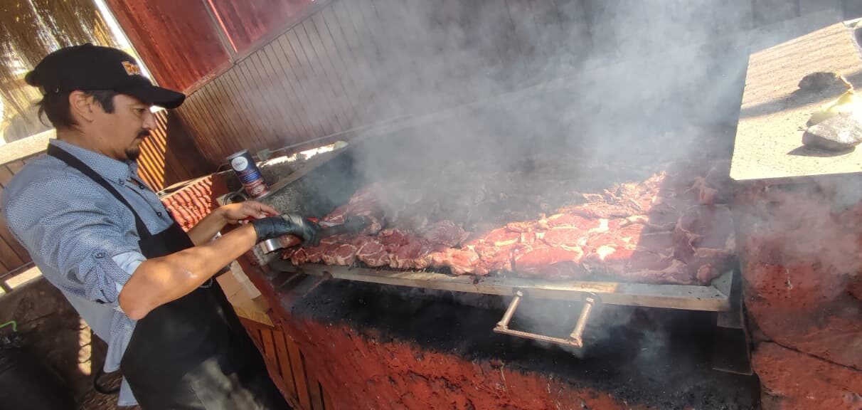 Maestro parrillero preparando carne al fuego en un evento Fogones